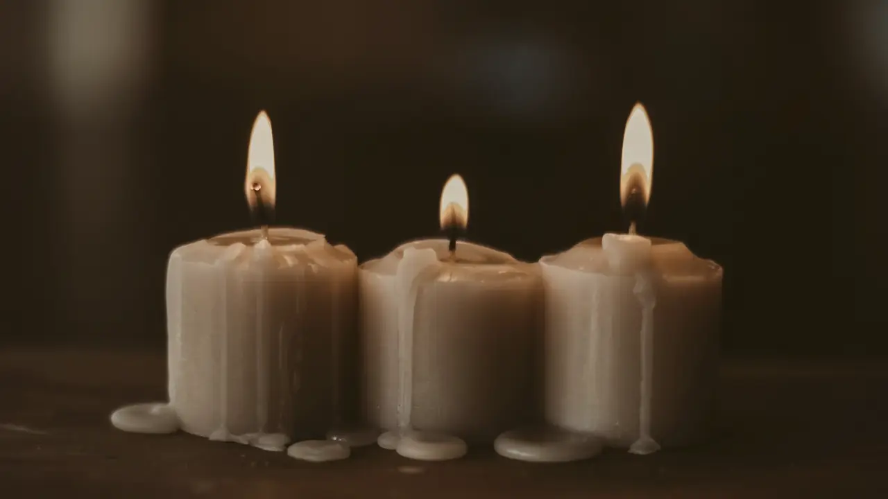 Three white candles burning steadily in a dark room